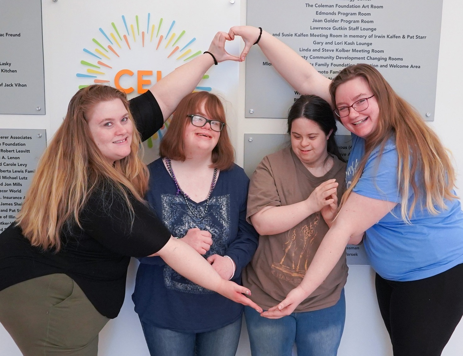 A group of CEL members smiling in front of logo with heart shaped hands.